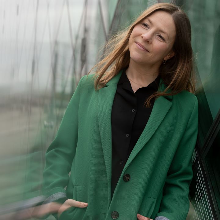 Maria Matthäus im grünen Mantel, lächelnd an ein Geländer gelehnt